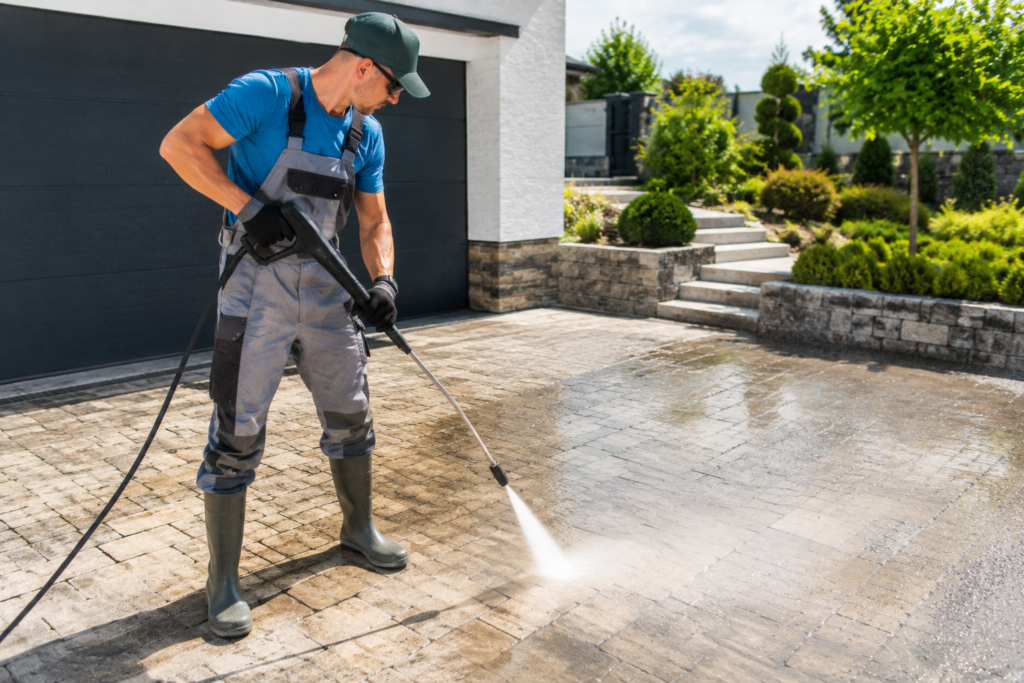 contractor pressure washing an outdoor stone floor in front of a modern house